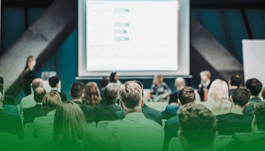 Personas asistiendo a una conferencia en un auditorio, con una ponente en el escenario y una pantalla de presentación proyectada al fondo. Personas asistiendo a una conferencia en un auditorio, con una ponente en el escenario y una pantalla de presentación proyectada al fondo.