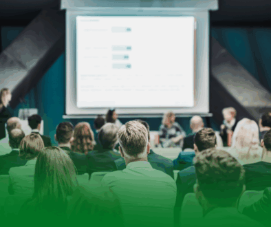 Personas asistiendo a una conferencia en un auditorio, con una ponente en el escenario y una pantalla de presentación proyectada al fondo. Personas asistiendo a una conferencia en un auditorio, con una ponente en el escenario y una pantalla de presentación proyectada al fondo.