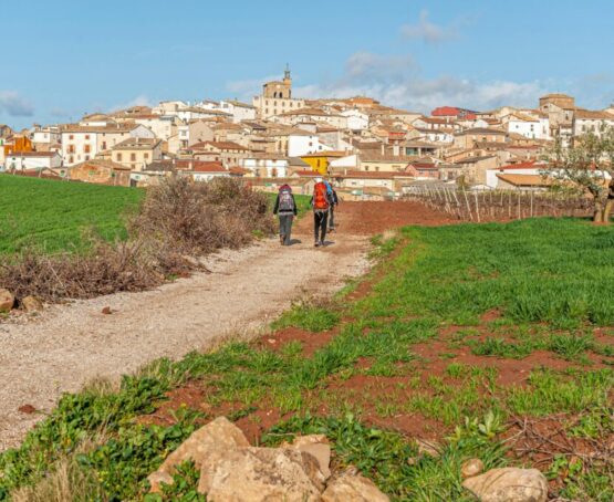 Dos personas caminando por un sendero hacia un pueblo con casas y una iglesia al fondo Dos personas caminando por un sendero hacia un pueblo con casas y una iglesia al fondo